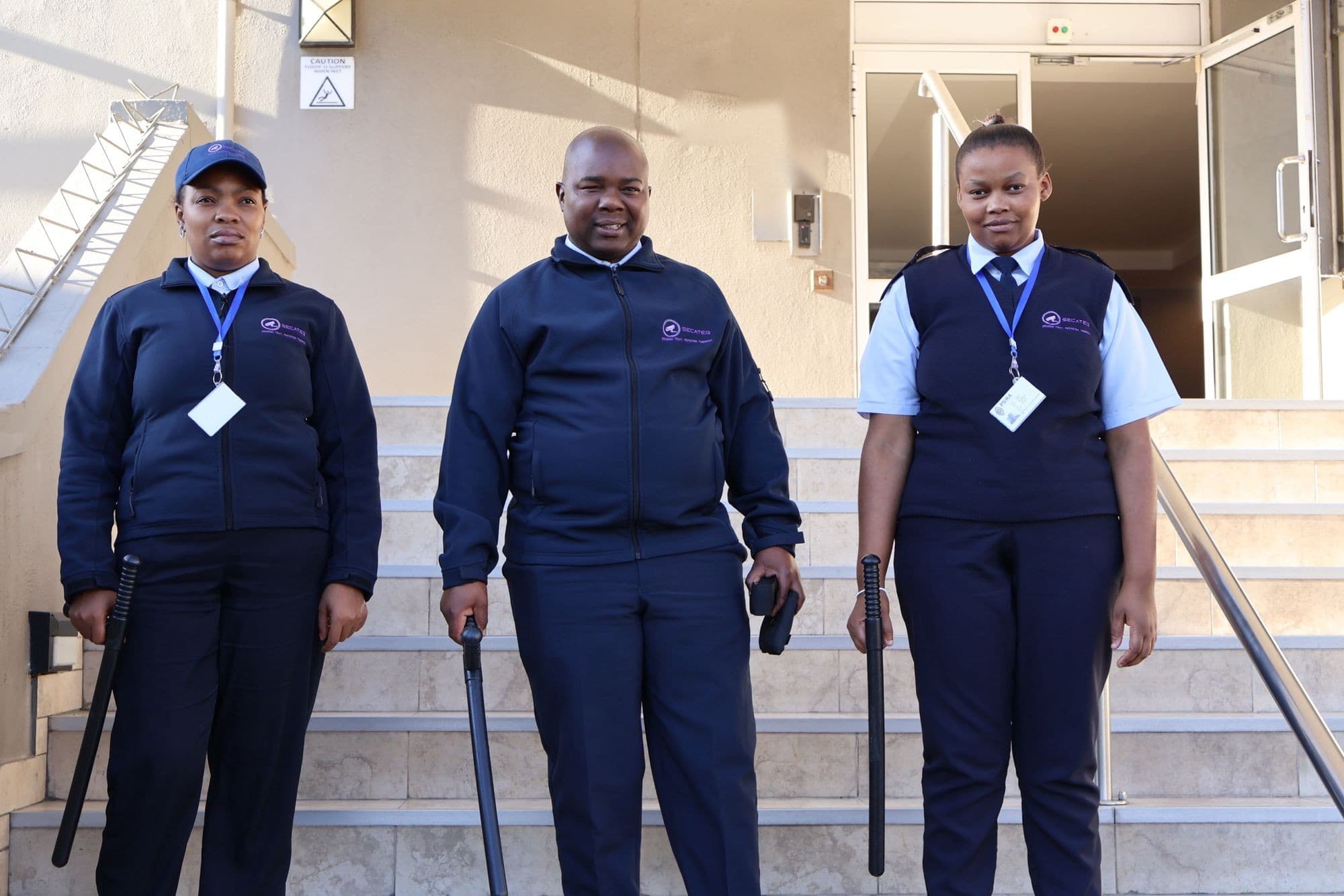 Three members of a SecaTeq concierge team on the stairs at a building entrance