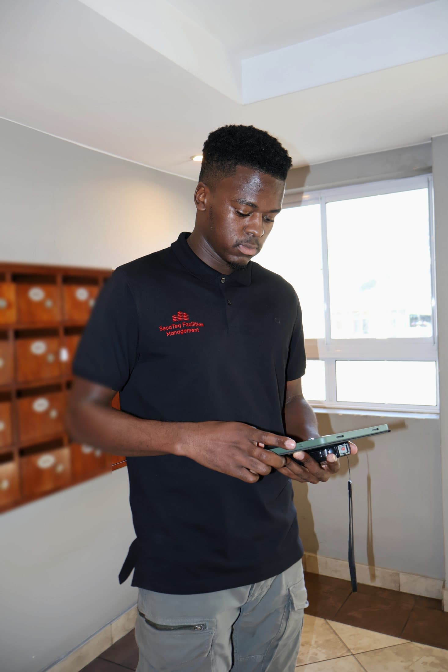 A SecaTeq FM technician in a residential lobby checking a work order on a tablet