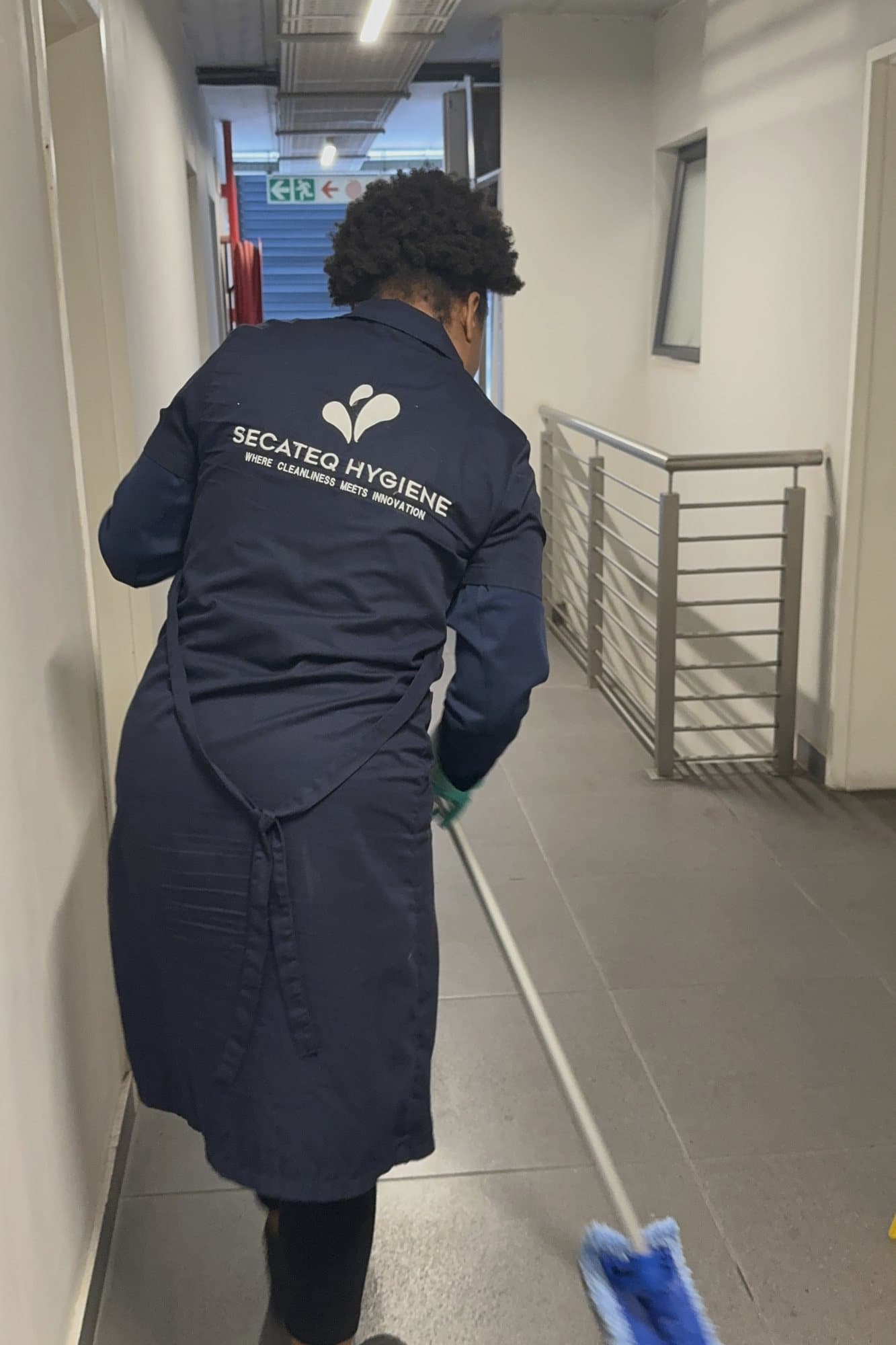A SecaTeq Hygiene team member mopping a corridor, the SecaTeq Hygiene wordmark on the back of her coat