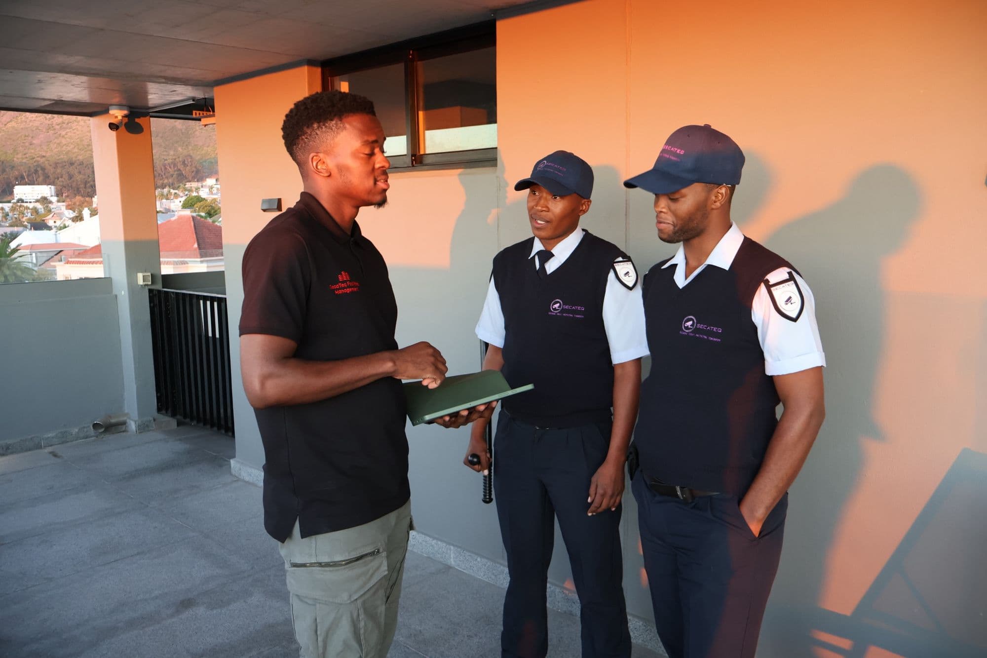 A SecaTeq FM technician with a folder, talking to two SecaTeq officers at golden hour