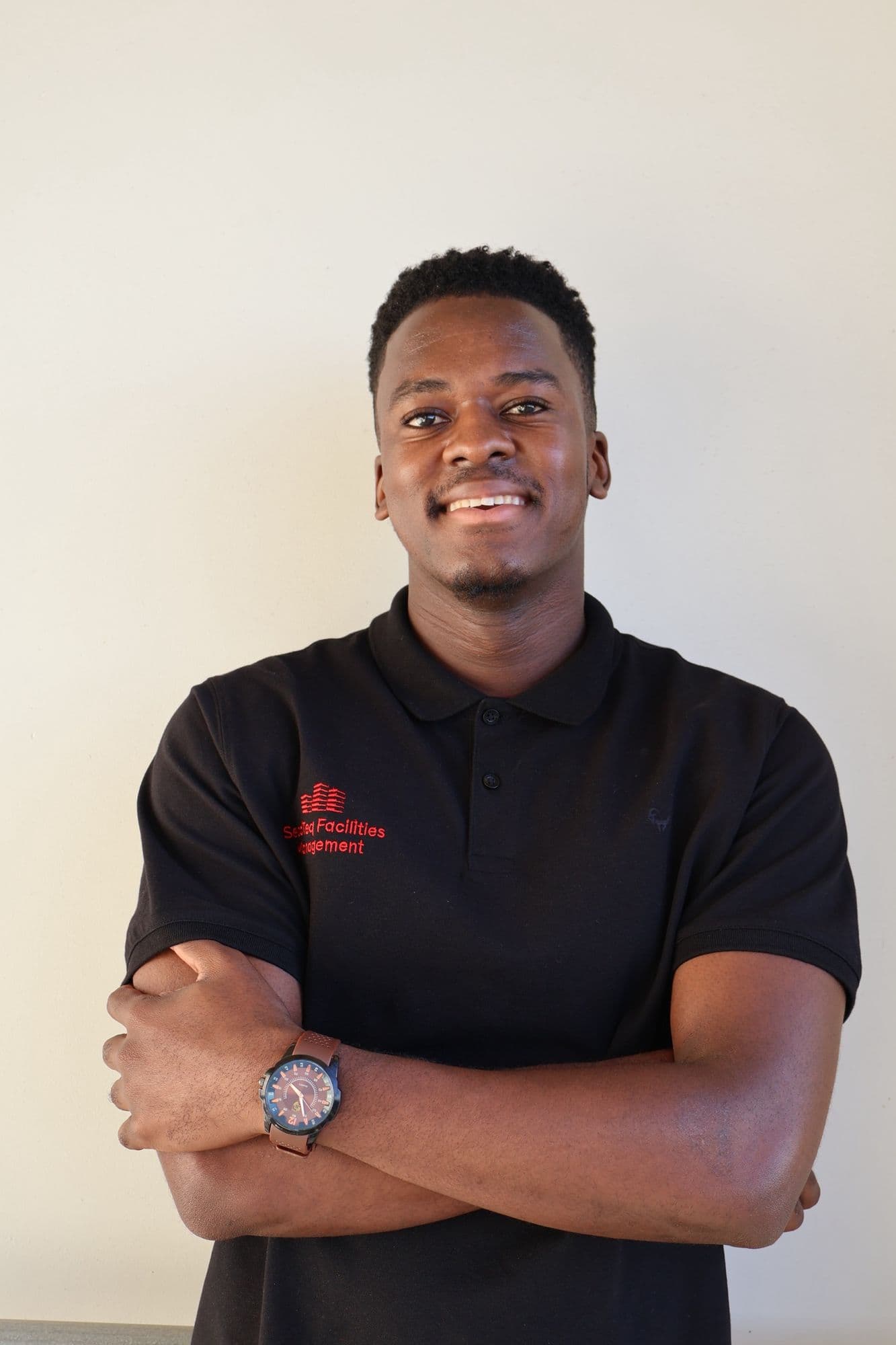A SecaTeq FM technician in the black polo with the red SecaTeq Facilities Management logo, arms folded