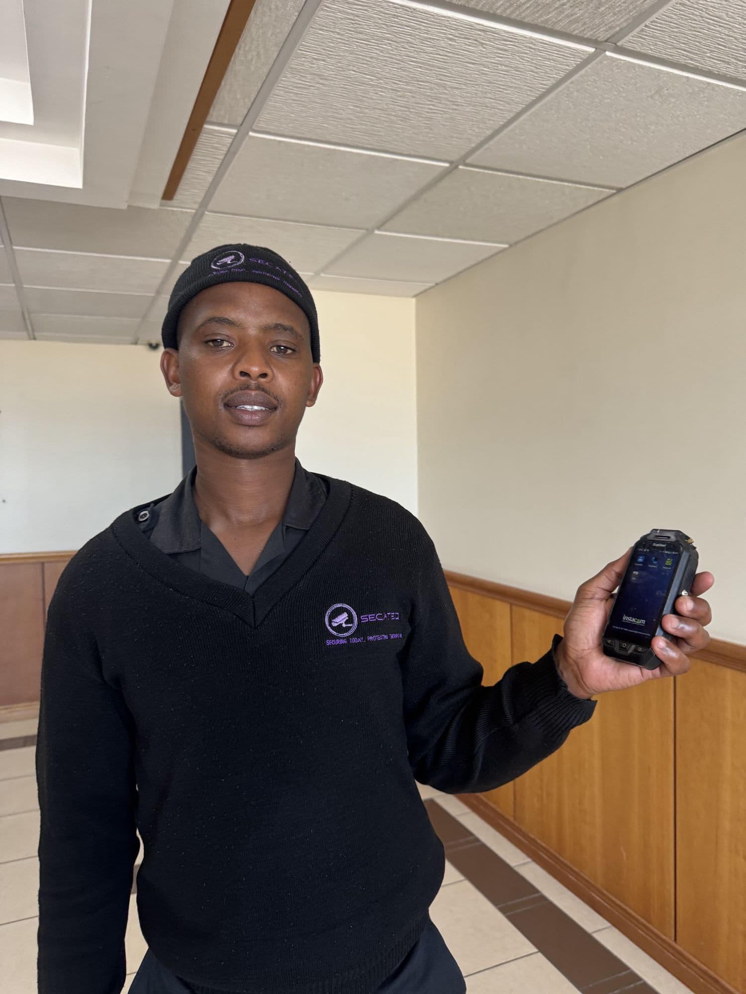 A SecaTeq officer holding up his handset in a building corridor