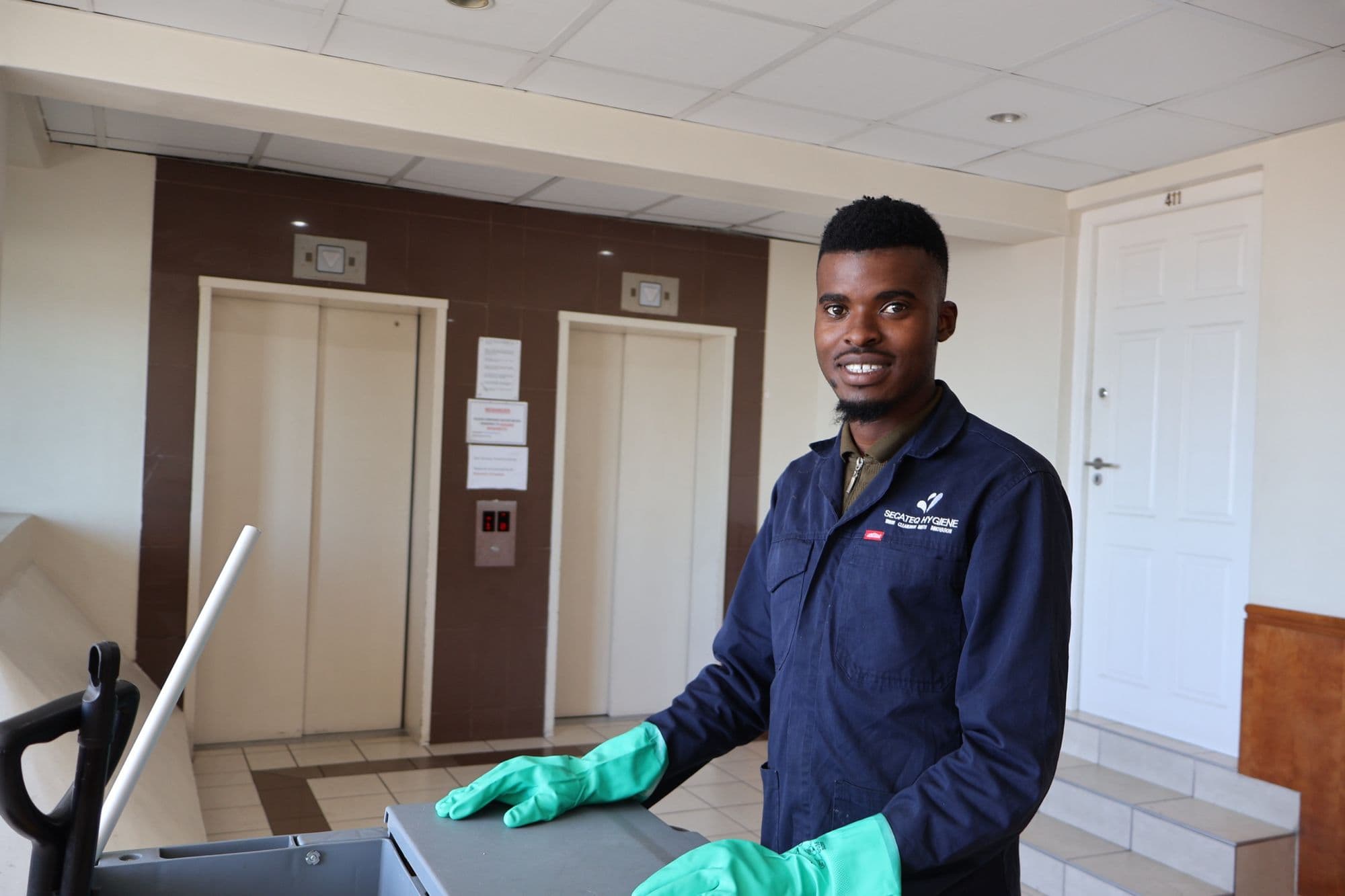 A SecaTeq Hygiene team member in gloves with a cleaning trolley in a lift lobby